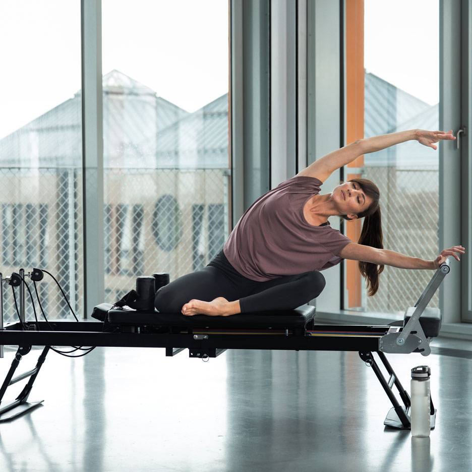 Kvinna som tränar pilates på en reformer-maskin, sträcker sig i sidled.