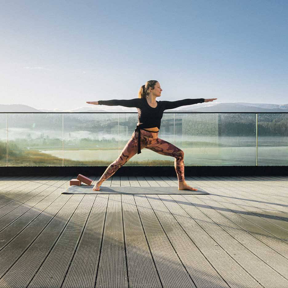 Kvinna i träningsleggings och topp gör yoga på en terrass med utsikt.
