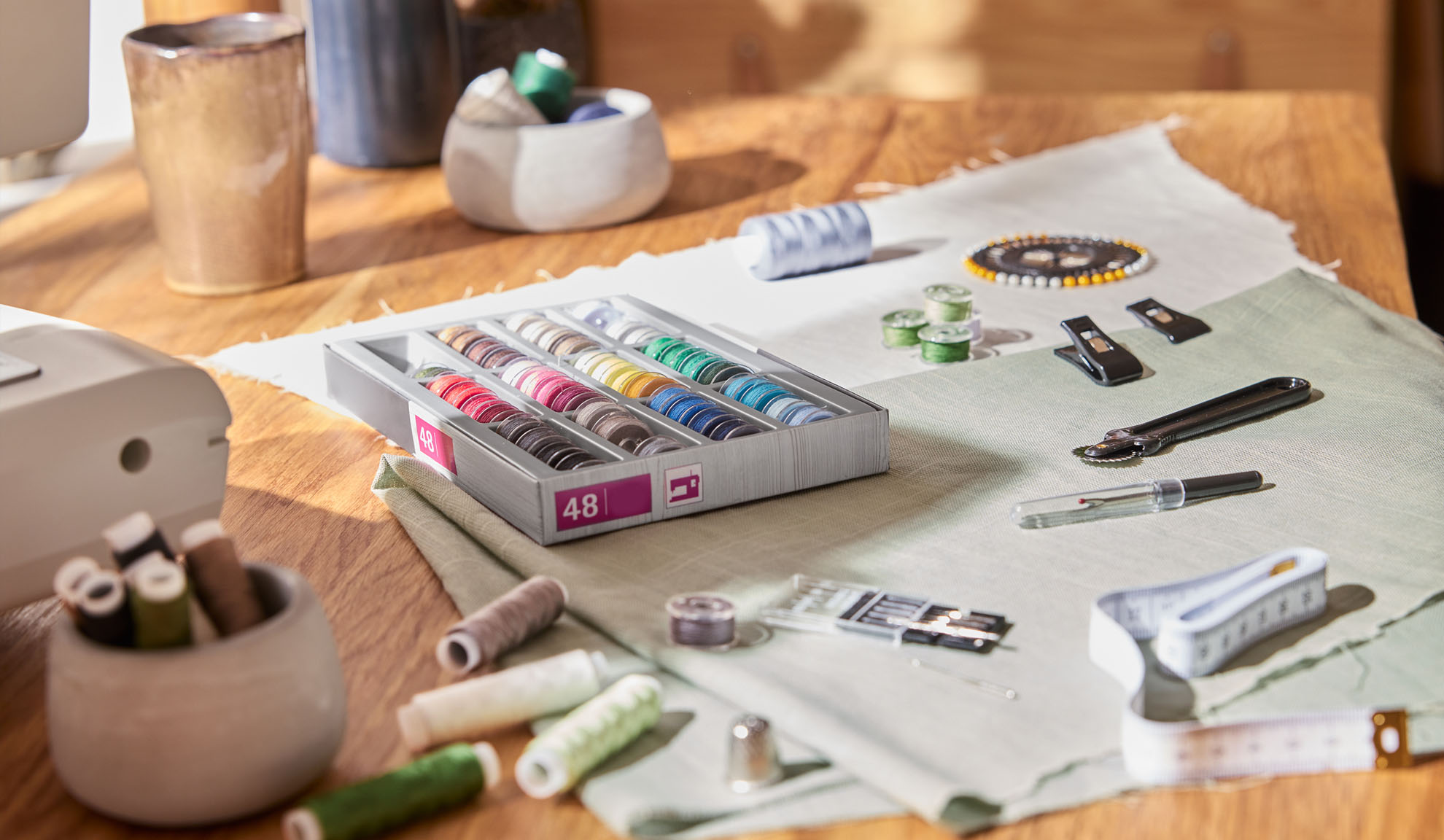 Sysats med en låda färgglada trådar, symaskin och olika verktyg på ett träbord.