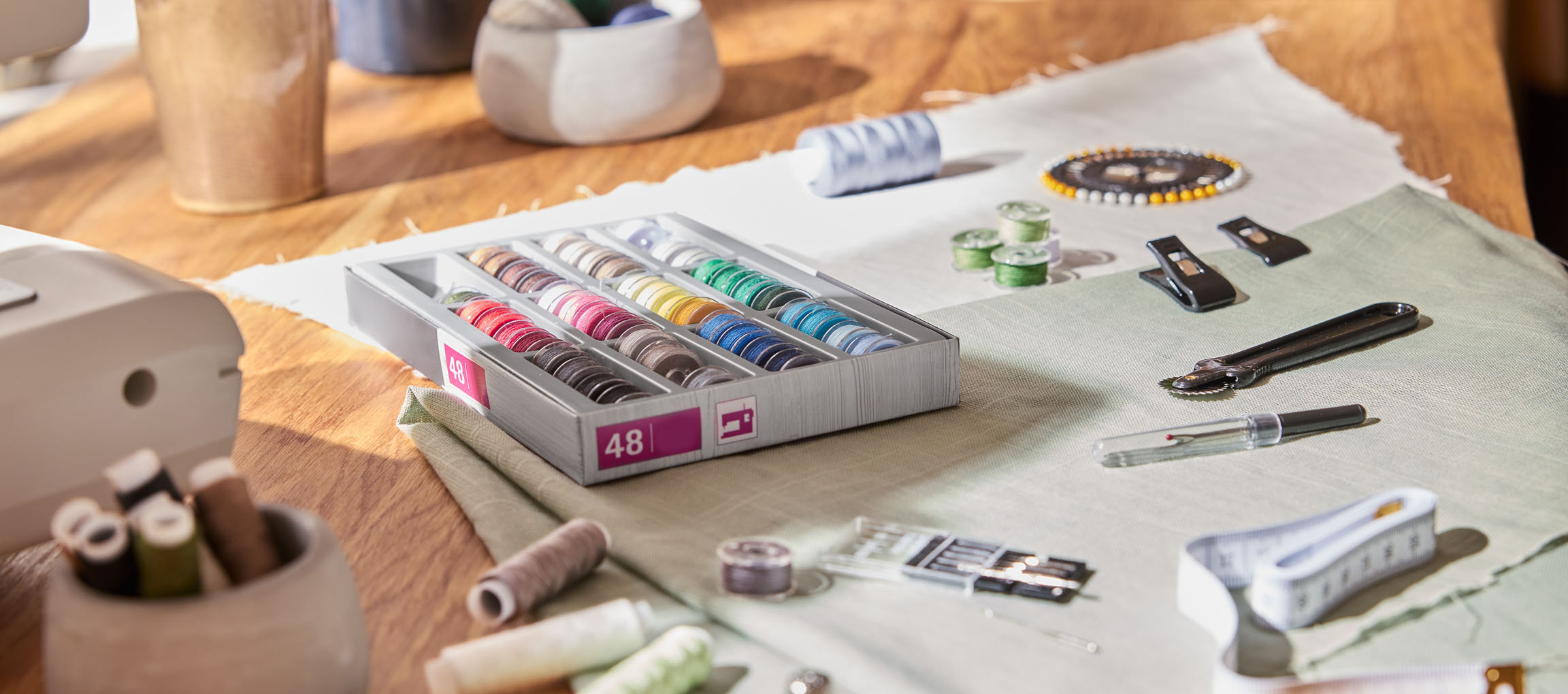 Syartiklar på ett träbord, inklusive en trådorganisatör med 48 spolar, tyg och olika verktyg.