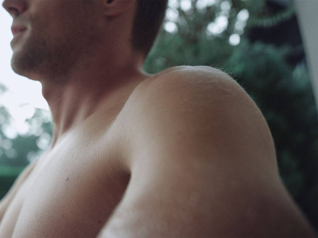 Närbild på en mans axel och hals, med suddig grön bakgrund.