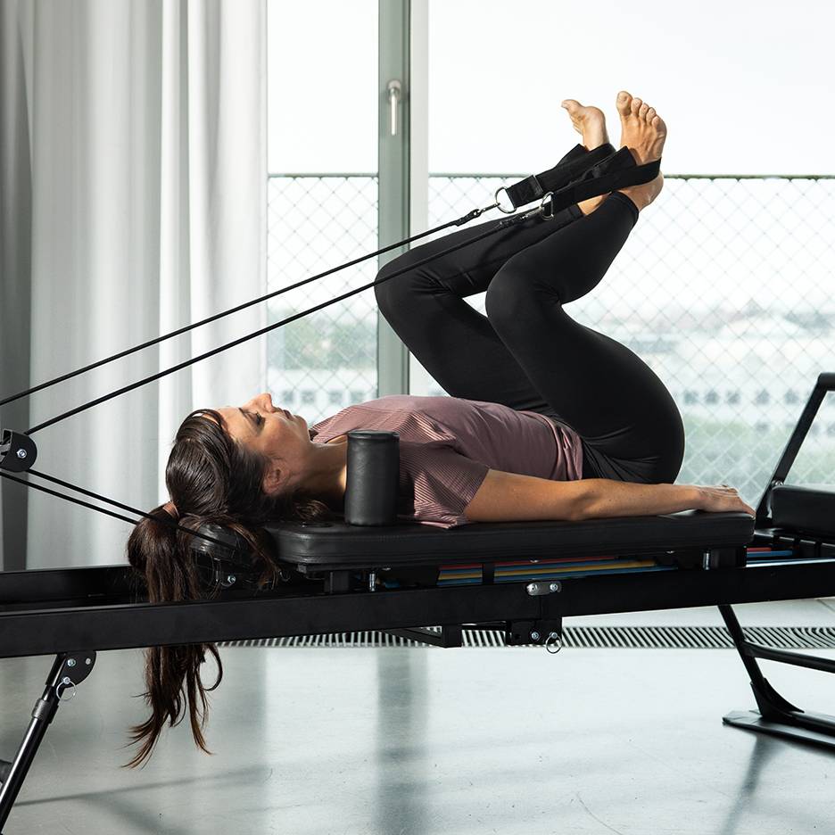 Kvinna tränar ben på en pilates reformer med motståndsband.