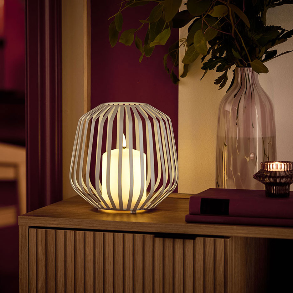 Ett LED-ljus i en vit metallhållare på en träbyrå.