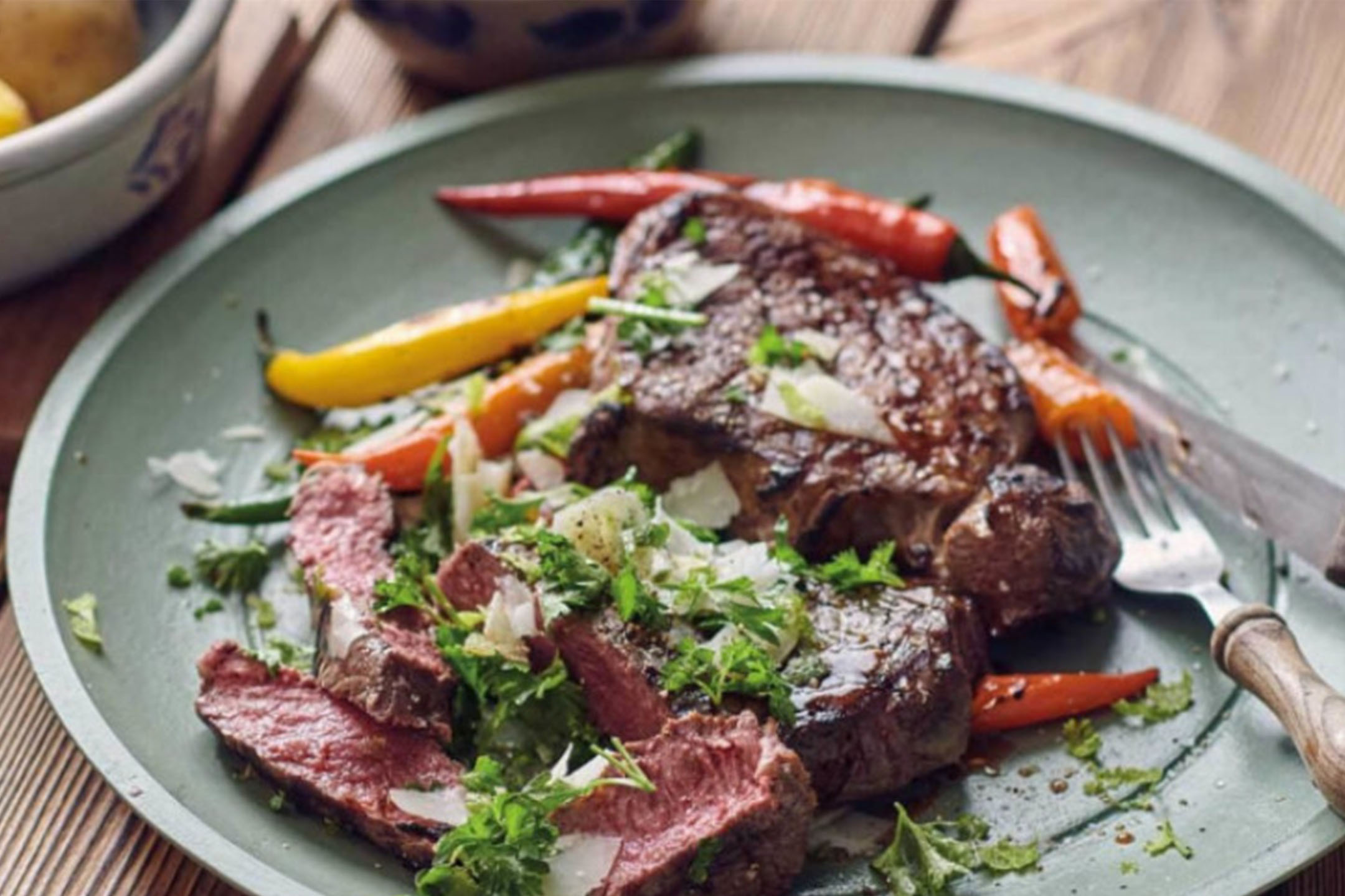 Grillad biff med paprika, färska örter och hyvlad ost på en grön tallrik.