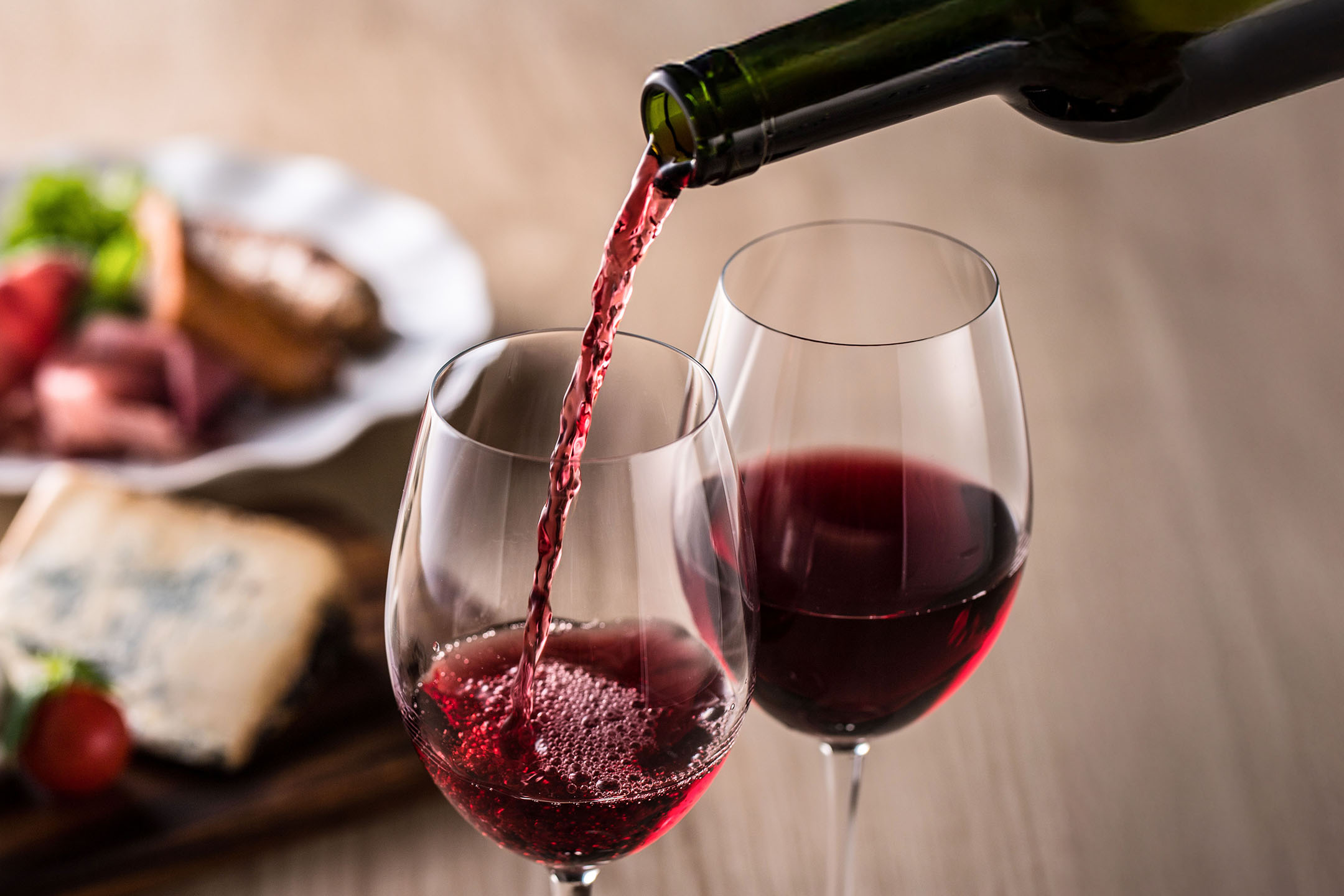Rödvin hälls i ett glas, med aptitretare i bakgrunden.