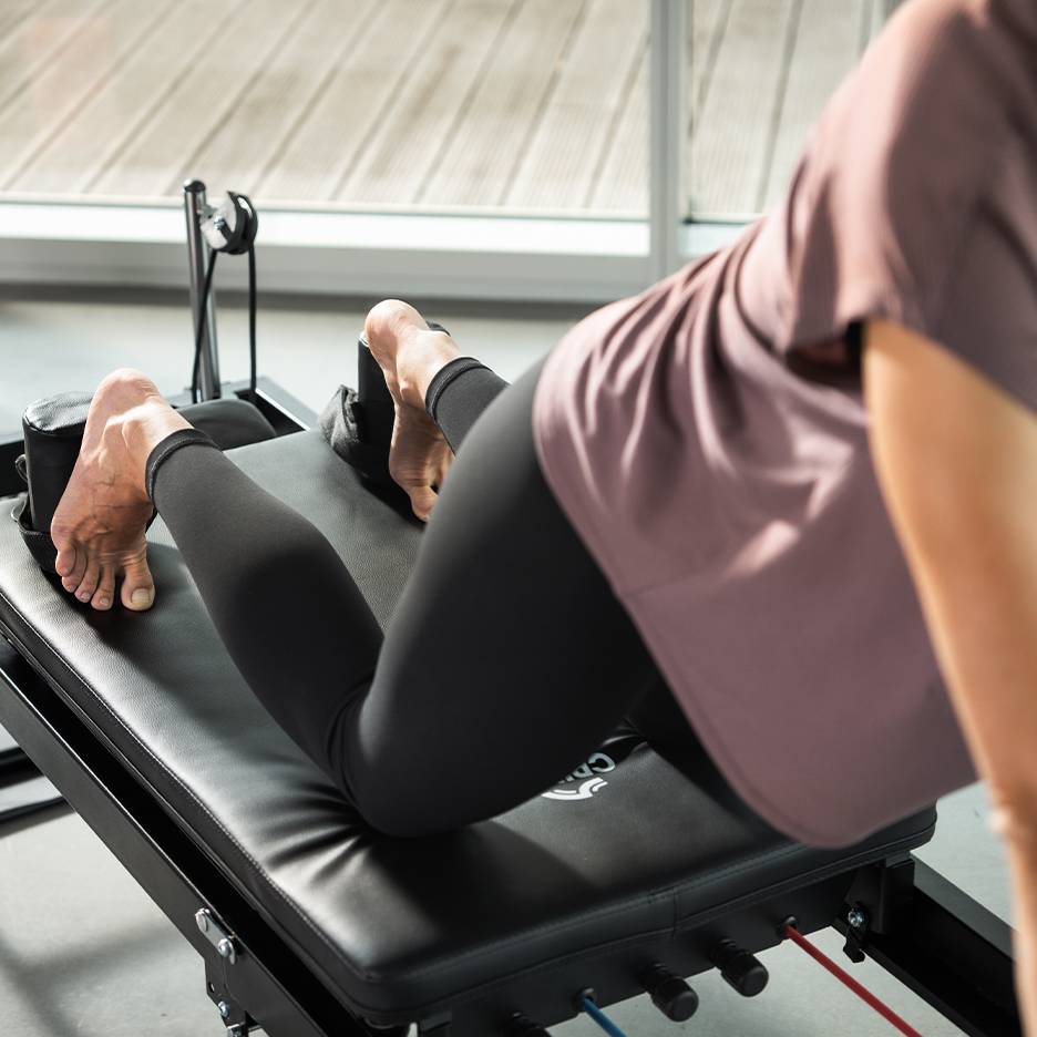 Kvinna tränar på en svart pilatesmaskin med fötterna i remmar.