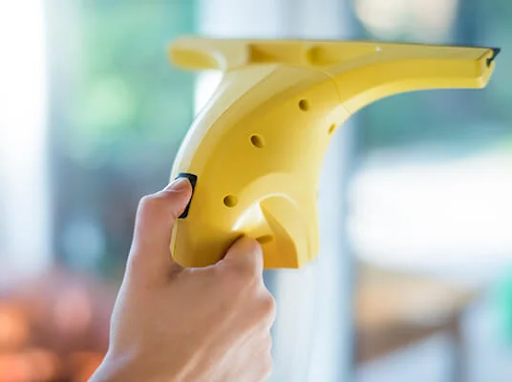 Hand håller en gul elektrisk fönstertvätt, rengör ett fönster.