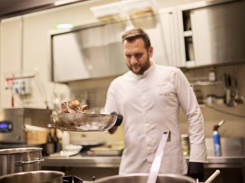 En kock i vit kockrock kastar mat i en panna.