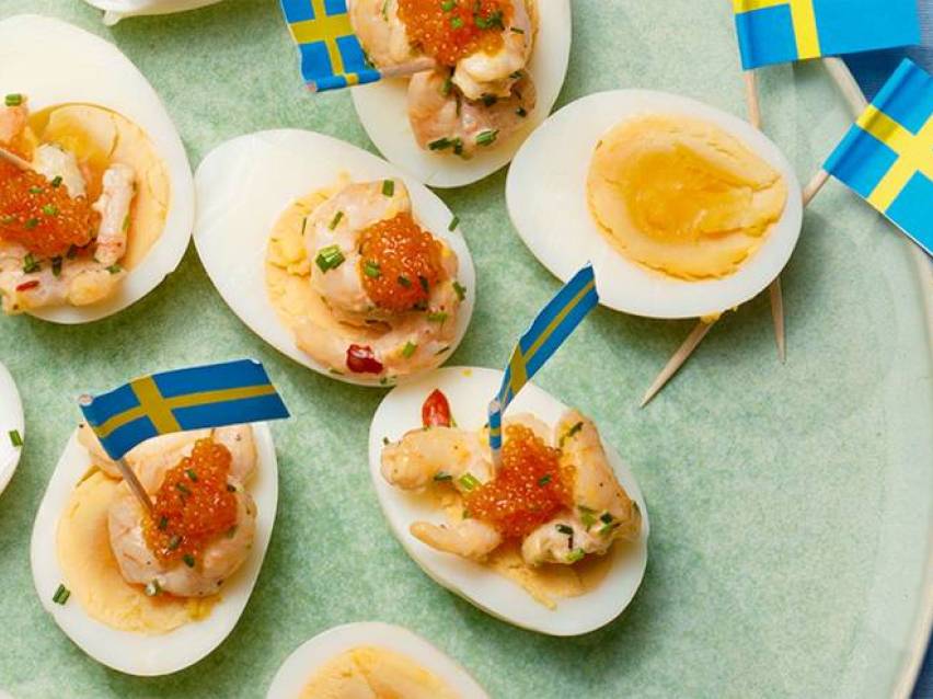 Halverade ägg med räkor, rom och svenska flaggor på en grön tallrik.