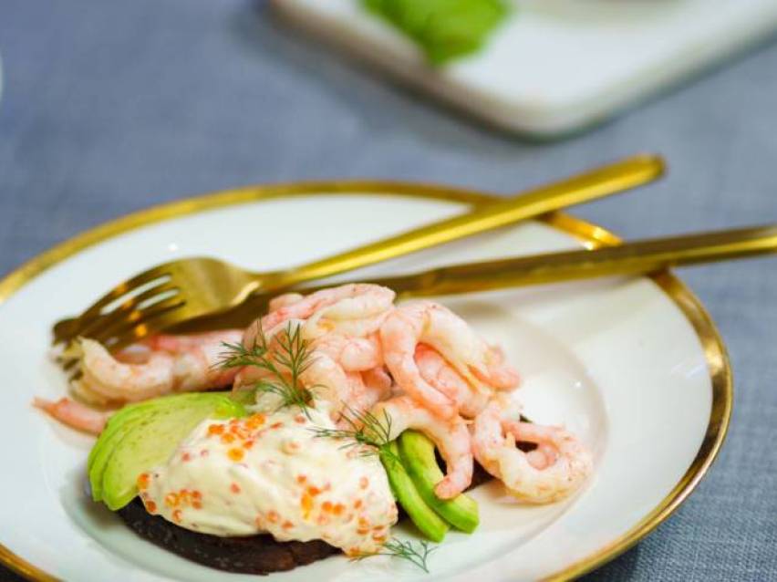 Räksmörgås med avokado, majonnäs och dill på en vit tallrik med guldkant.