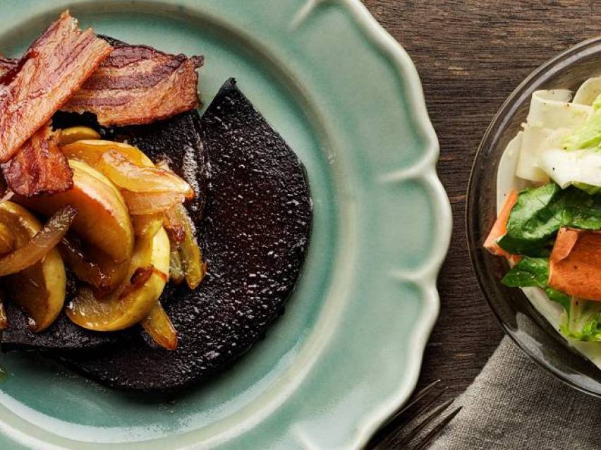 Stekt bacon, äpplen och lök på en mörk skiva, med en sallad bredvid.