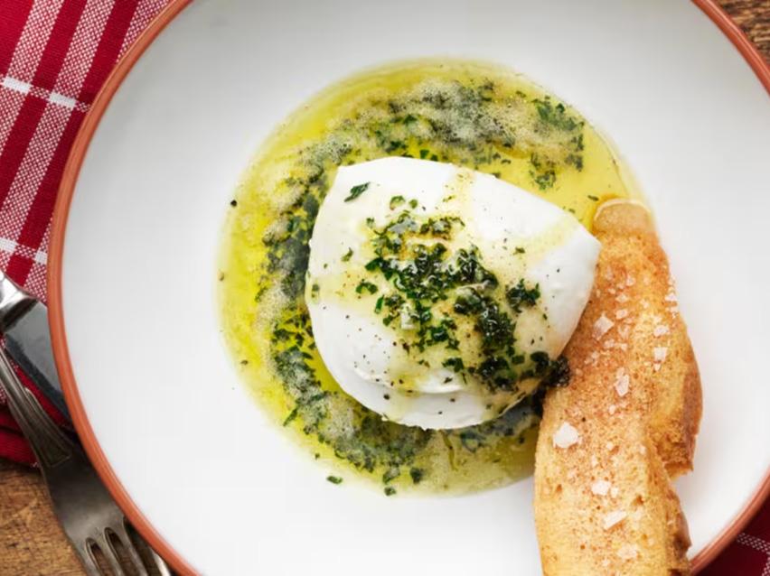 Krämig burrata serverad med örtolja och krispigt bröd på en tallrik.