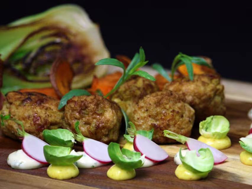 Närbild på köttbullar med grönsaker och såser på en träskärbräda.