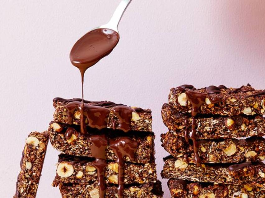 Chokladöverdragna müslibars med nötter, där smält choklad ringlas över från en sked.