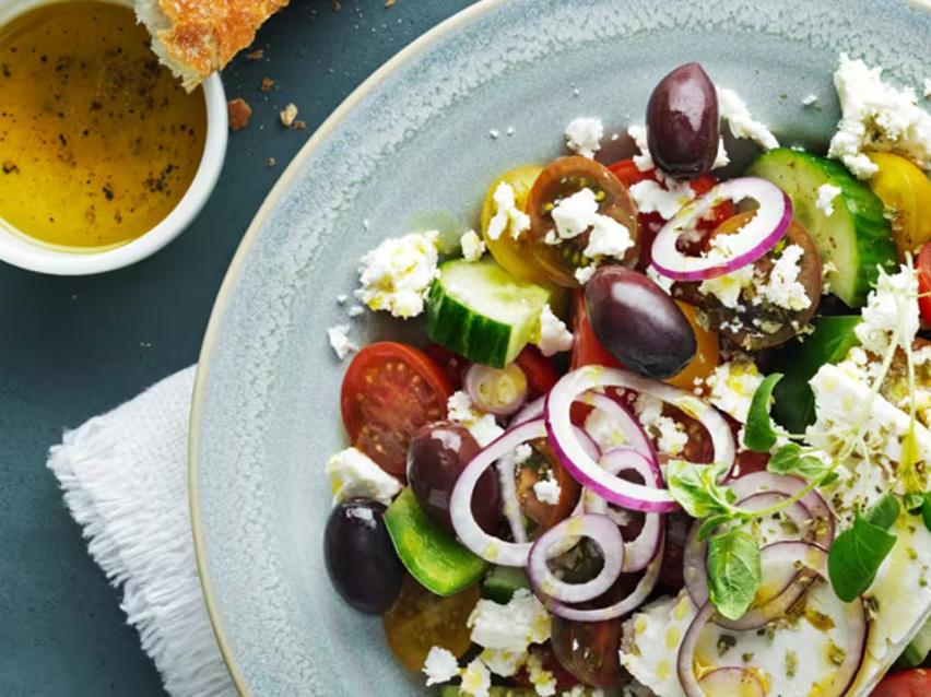 Grekisk sallad med tomater, gurka, rödlök, oliver och fetaost, serverad med dressing och bröd.