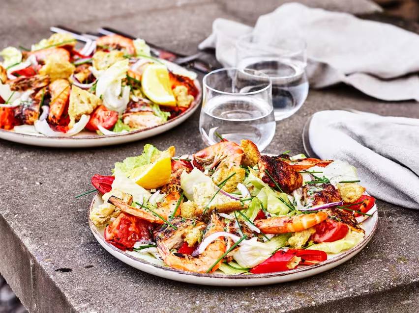Två tallrikar med sallad med räkor, kyckling, krutonger, grönsaker och citronklyftor.