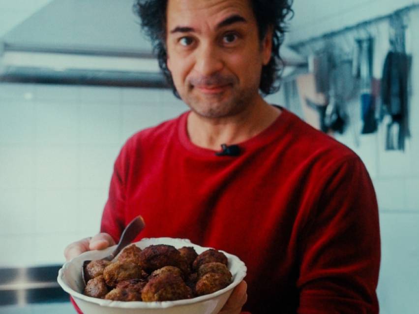 Man i röd tröja håller en skål med köttbullar.