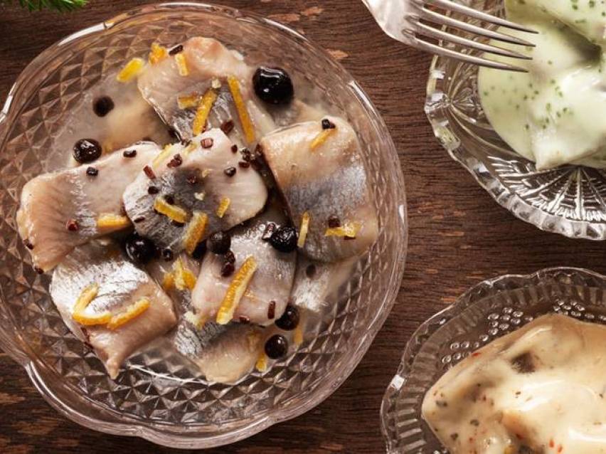 Inlagd sill med apelsinskal och svarta vinbär i en glasskål.