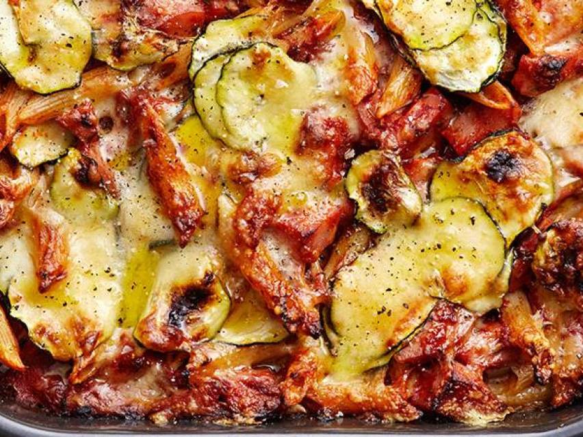 En närbild av en gratäng med zucchini, pasta och smält ost, toppad med svartpeppar.