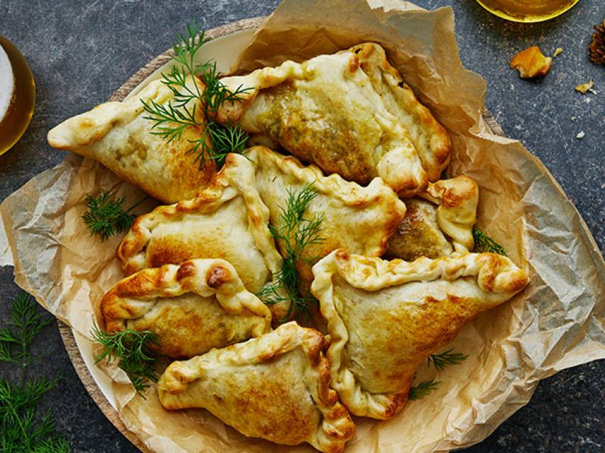 En tallrik med gyllenbruna empanadas med dillkvistar på bakplåtspapper.