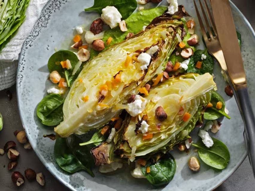 Grillad romansallad med spenat, hasselnötter, fetaost och morotsbitar på en tallrik.