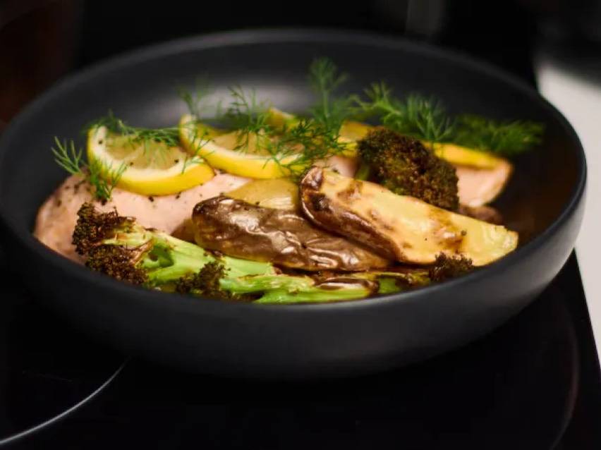 Lax med potatis, broccoli, citron och dill i en svart skål.