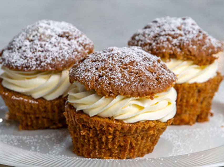 Tre morotsmuffins med gräddostfrosting och florsocker på en vit tallrik.