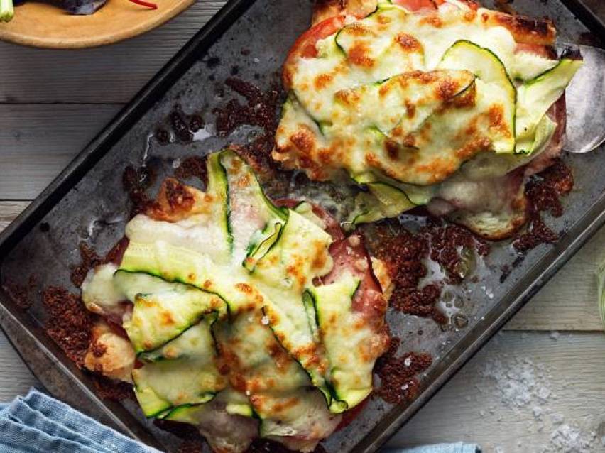 Ugnsbakad kyckling med zucchini och smält ost på en plåt.