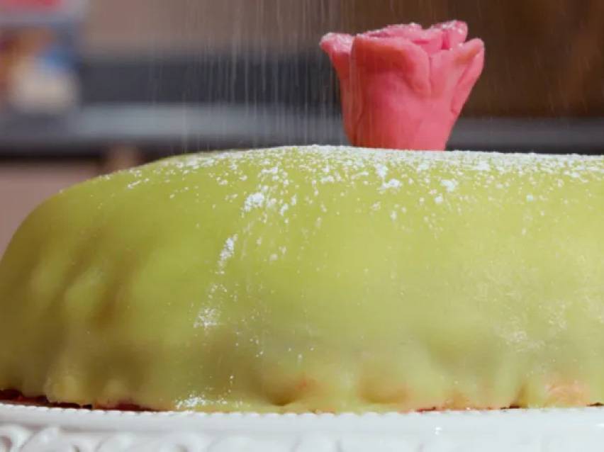 Prinsesstårta med grön marsipan, pudrad med florsocker och toppad med en rosa marsipanros.