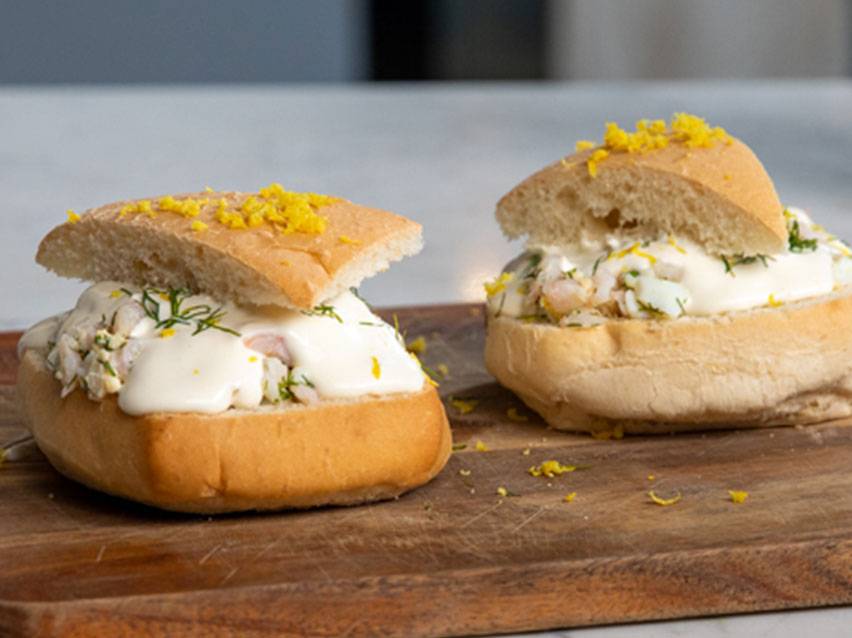 Två fyllda bröd med räkröra, majonnäs, dill och citronskal på en träskärbräda.