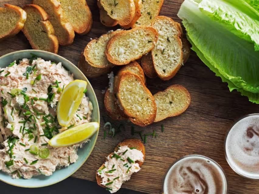 Fiskpaté med gräslök och citronklyftor, serverad med rostat bröd, sallad och öl.
