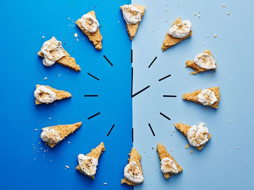 Klocka gjord av kakbitar med grädde och strössel på en blå bakgrund.