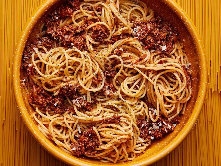Spaghetti bolognese i en gul skål, med rå spaghetti i bakgrunden.