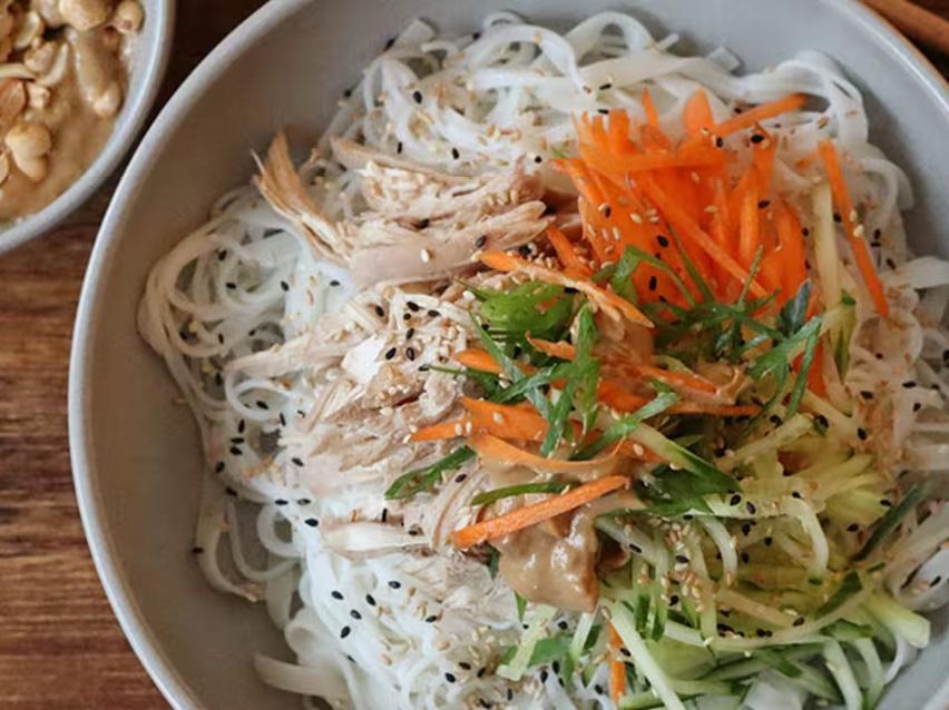 Nudelsallad med kyckling, morötter, gurka och sesamfrön i en skål.