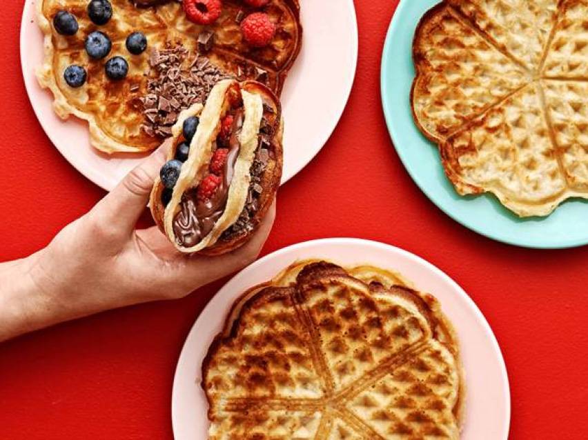 Våfflor med bär, choklad och Nutella, en hand håller en våffeltaco.