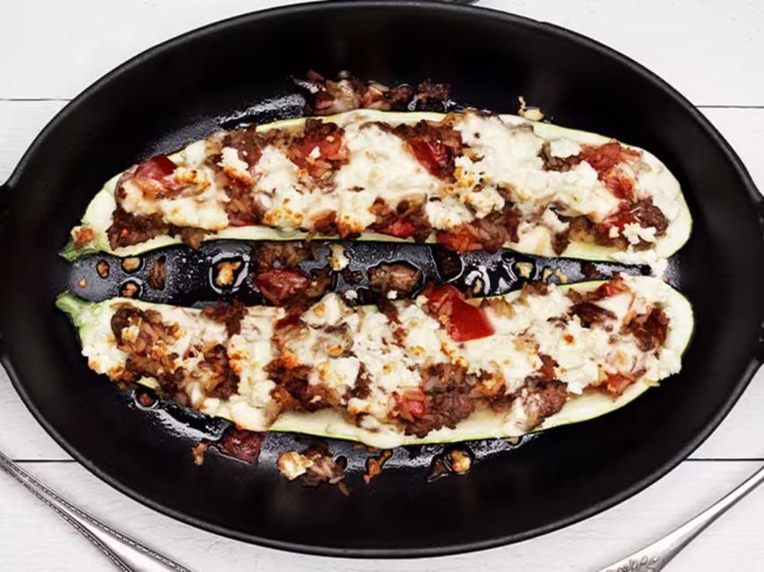 Fylld zucchini med köttfärs och ost i en svart gjutjärnspanna.