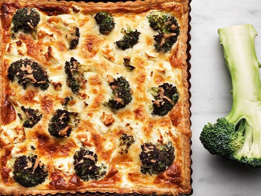 En rektangulär broccolipaj med en bit rå broccoli bredvid på en vit yta.