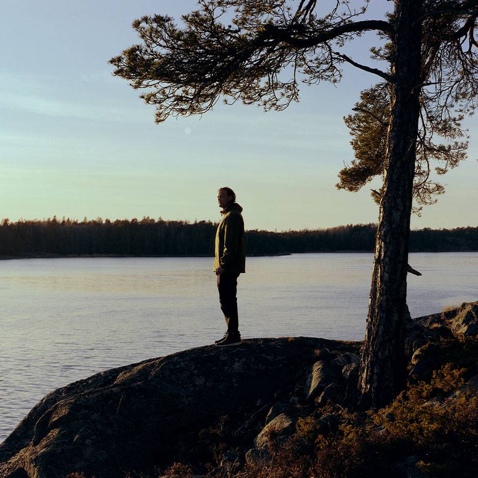 Man i vandringsjacka vid en sjö, med ett träd i förgrunden.