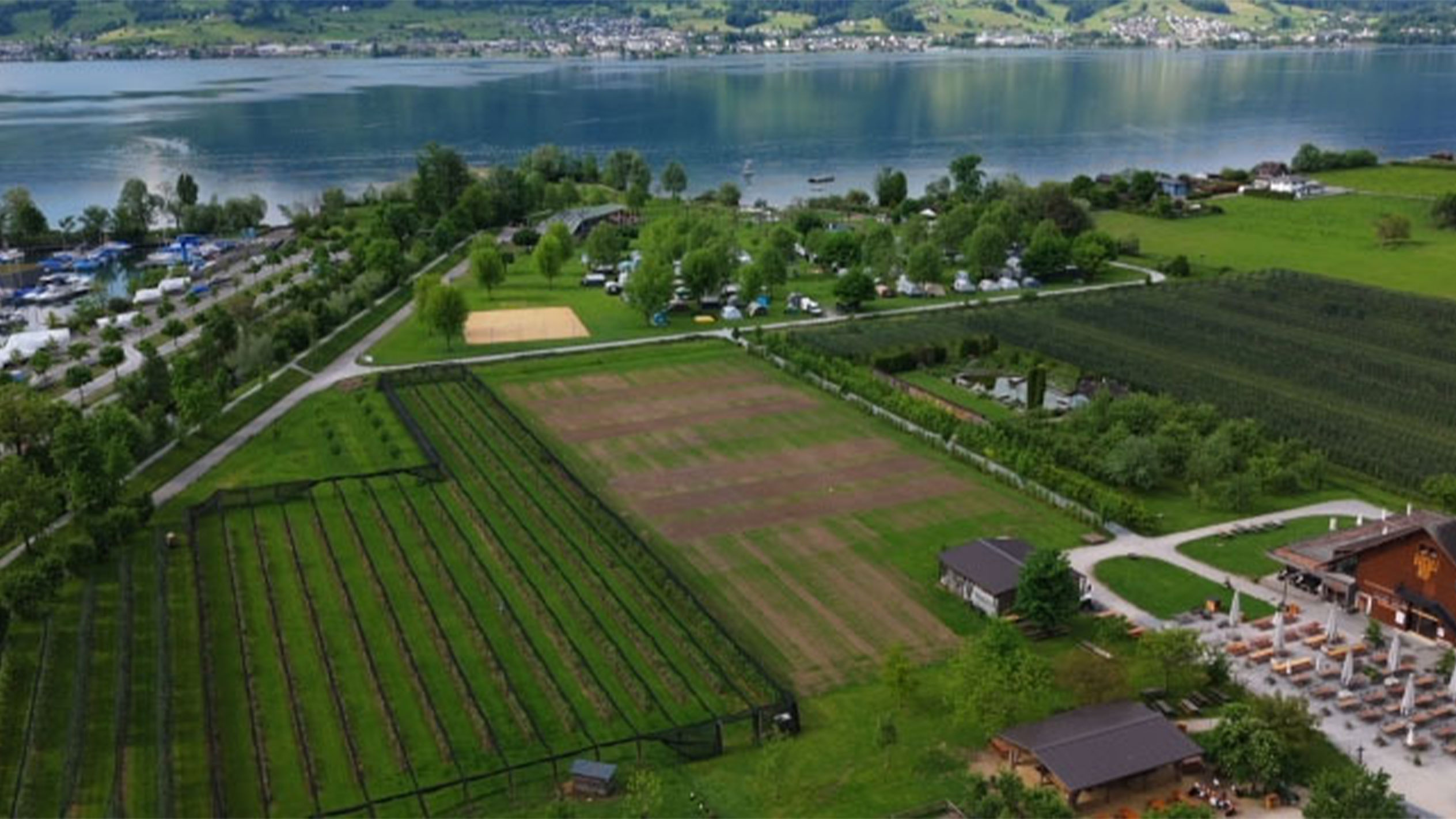 Flygfoto över en camping vid en sjö, med odlingar och en restaurang.