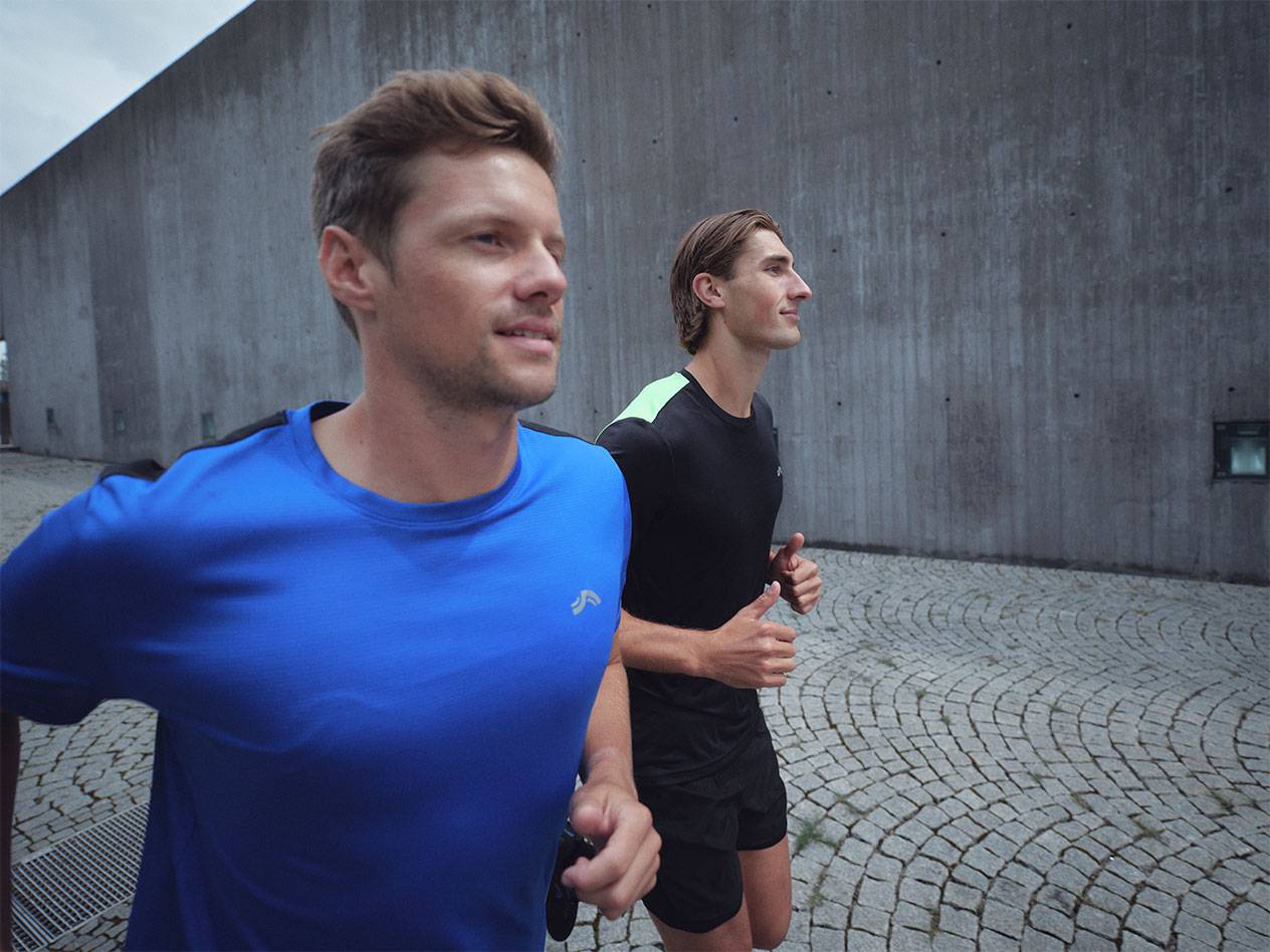 Två män springer i sport-t-shirts och shorts, en blå och en svart.