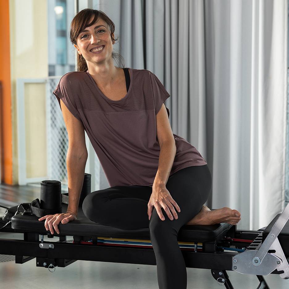 Kvinna i träningskläder sitter på en pilatesmaskin och ler.