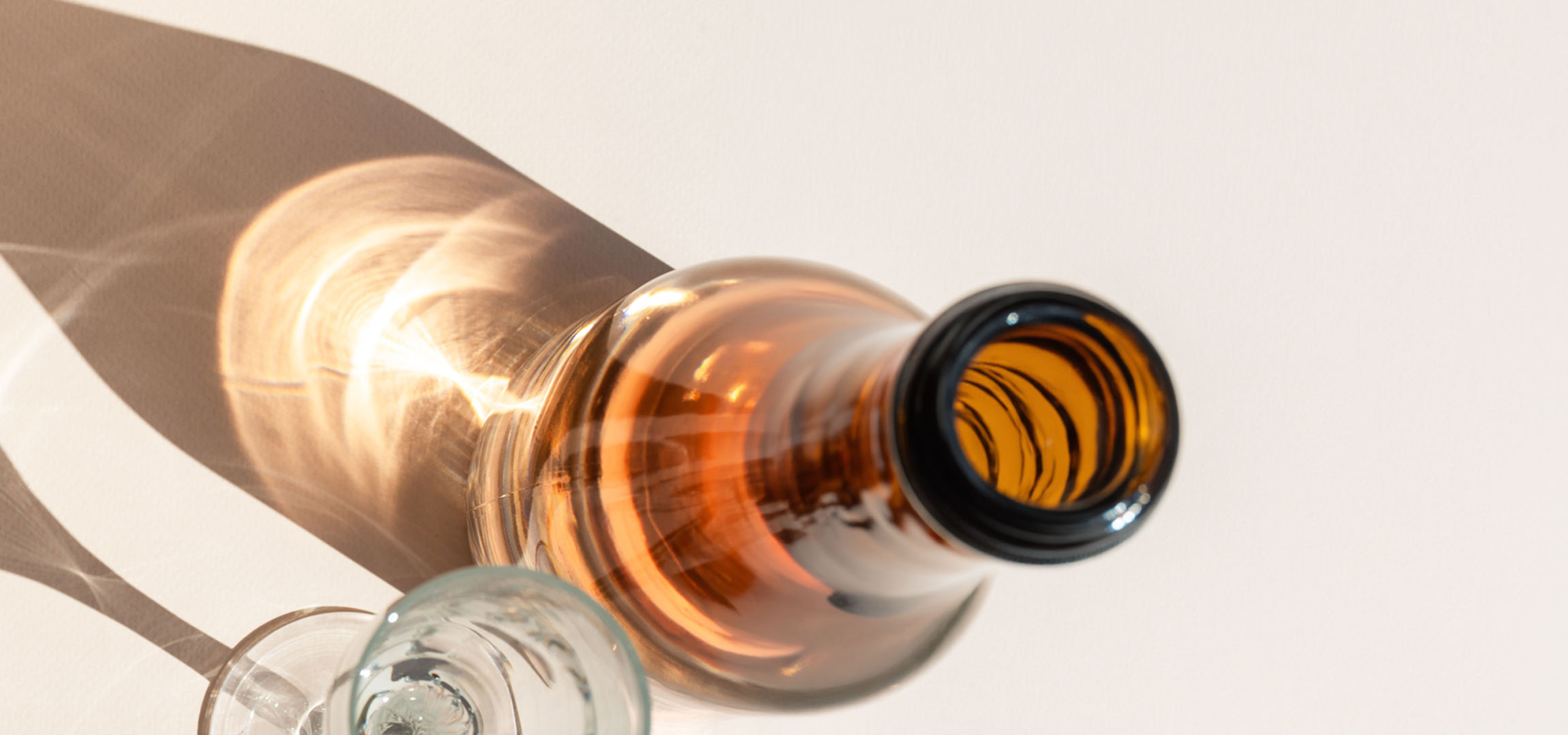 Glas och flaska med skuggor och ljusreflektioner på en ljus bakgrund