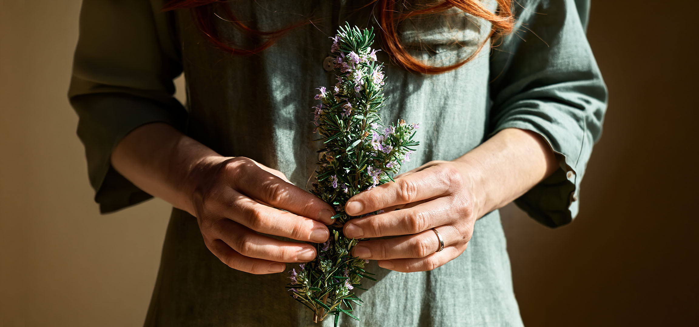 Kvinna i grön klänning håller blommande rosmarin.