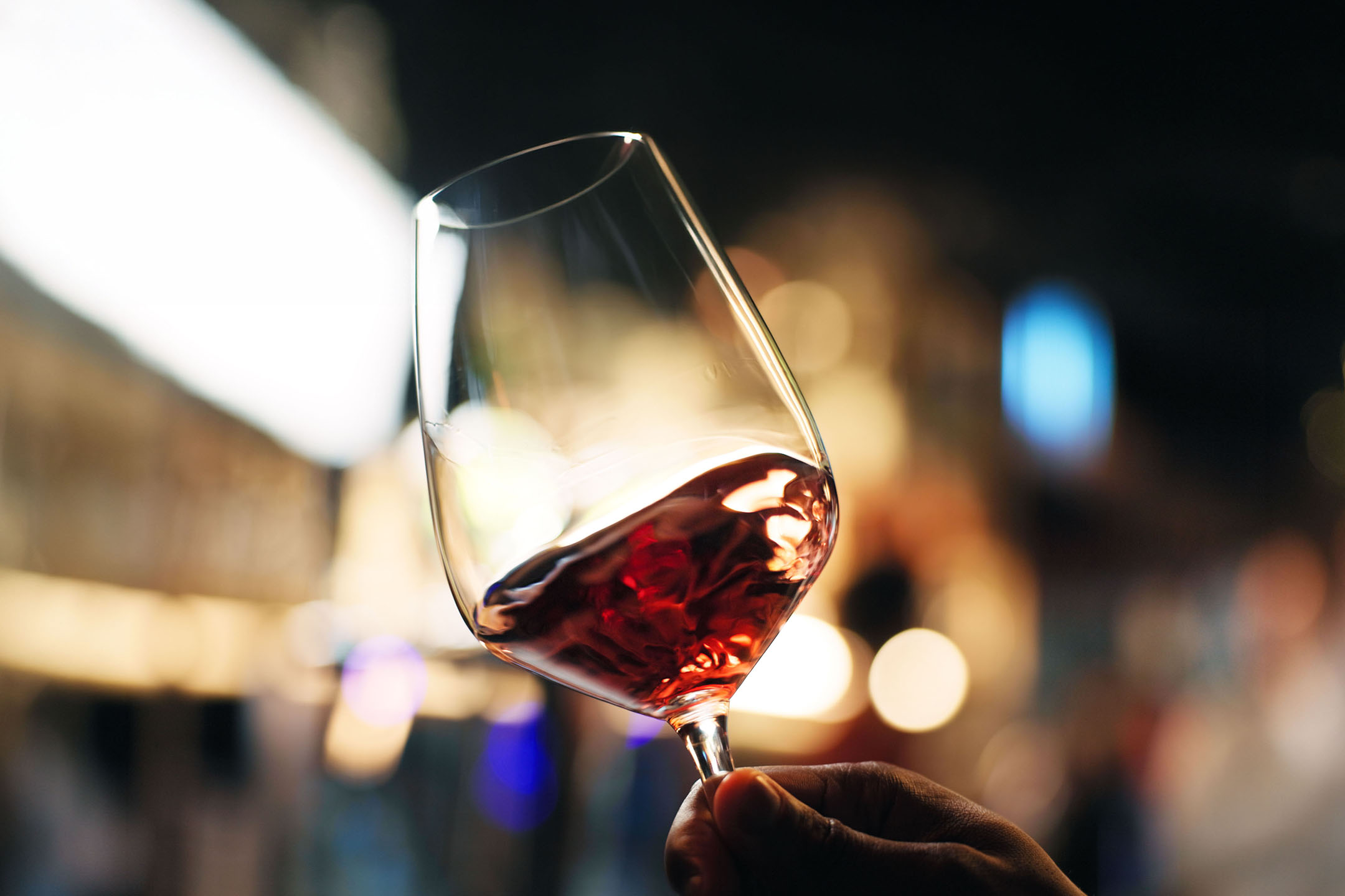 Glas rött vin hålls i handen, med suddiga ljus i bakgrunden.
