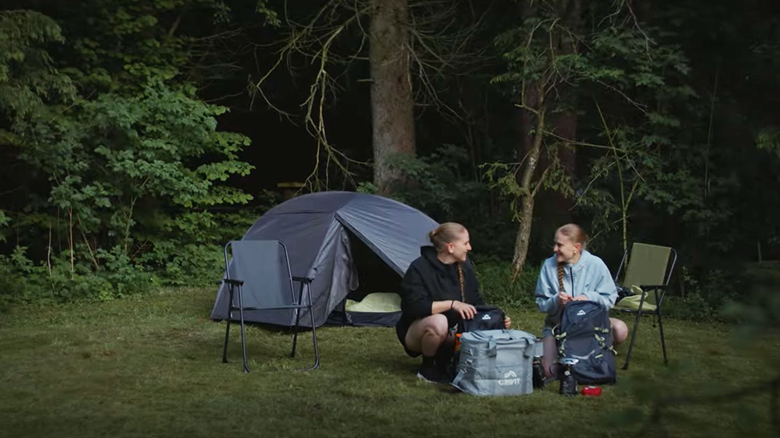 Två kvinnor campar med ett Crivit-tält och hopfällbara stolar.