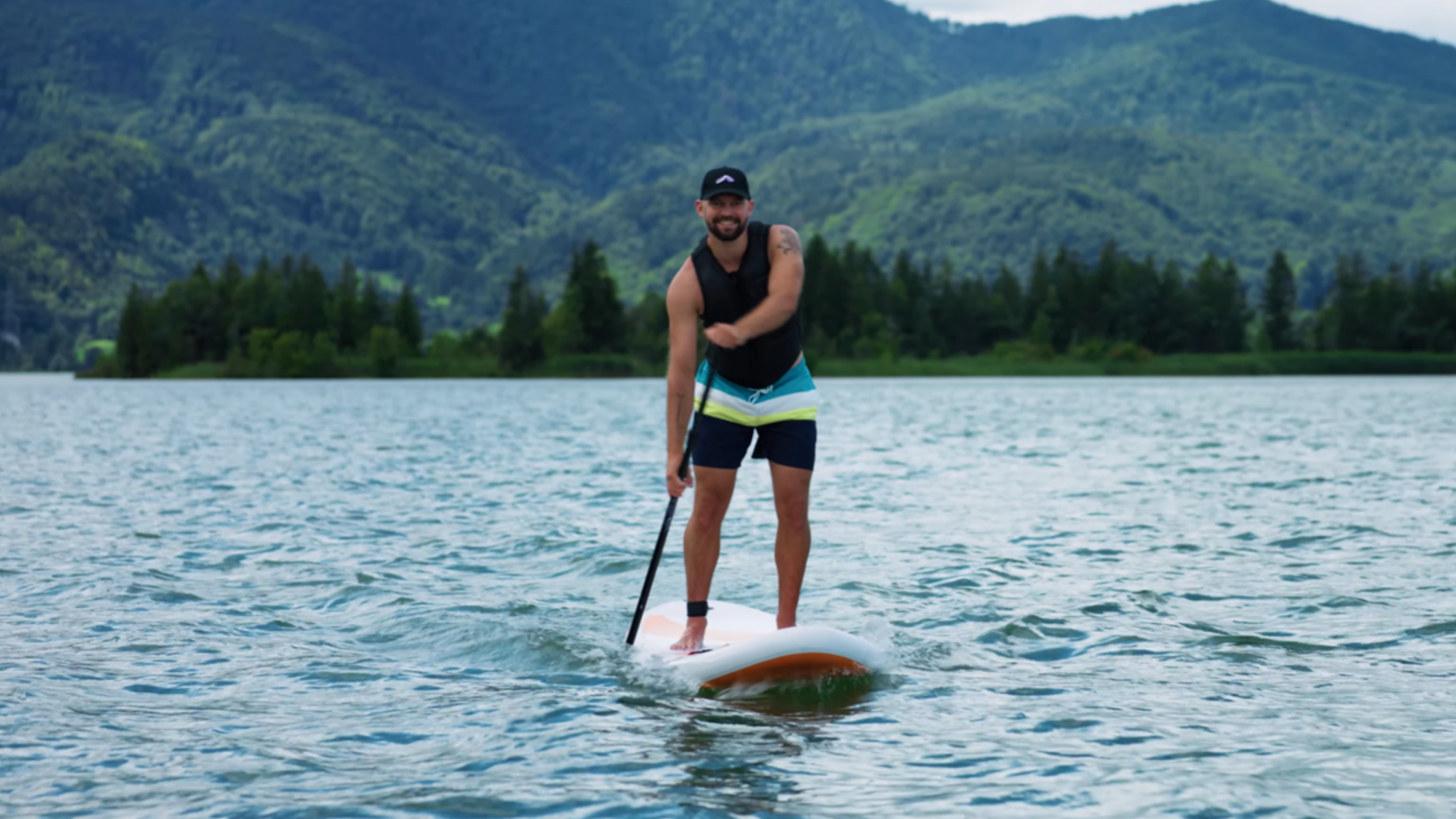 Man på paddleboard på en sjö med berg i bakgrunden.