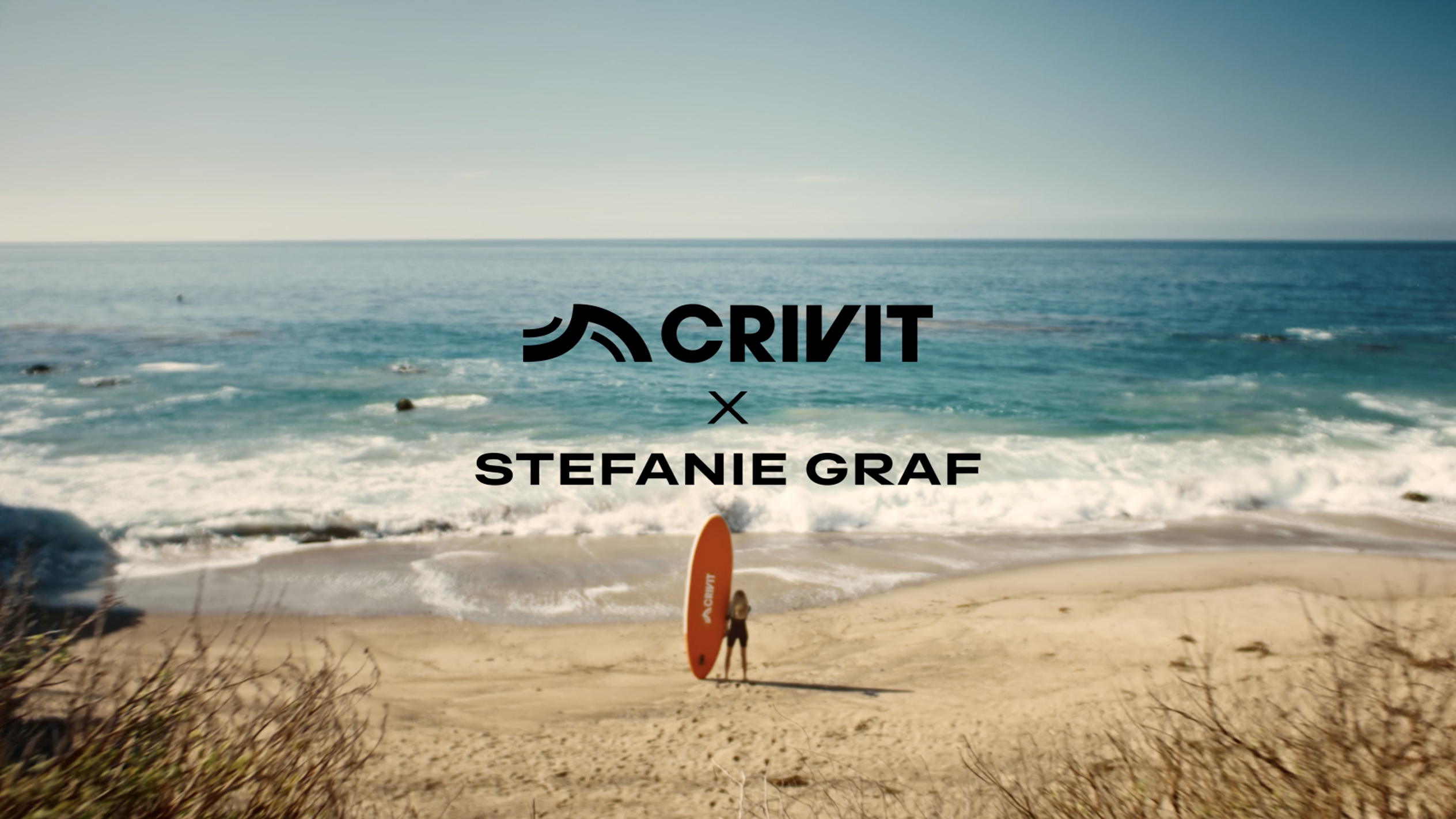 Kvinna med en orange SUP-bräda på en sandstrand, med havet i bakgrunden.