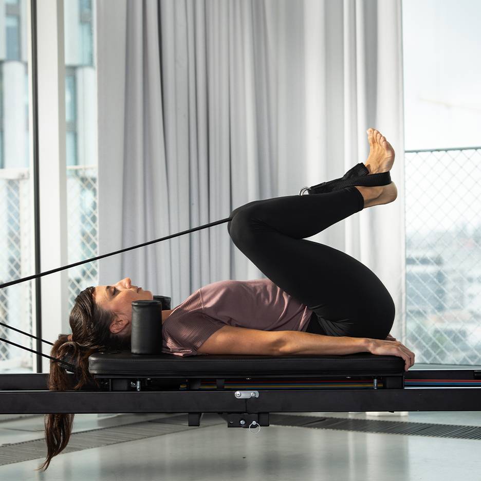 Kvinna tränar pilates på en reformer med benen uppåt.