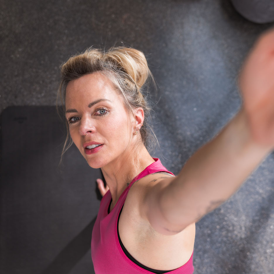 En kvinna i rosa träningstopp tar en selfie på gymmet.