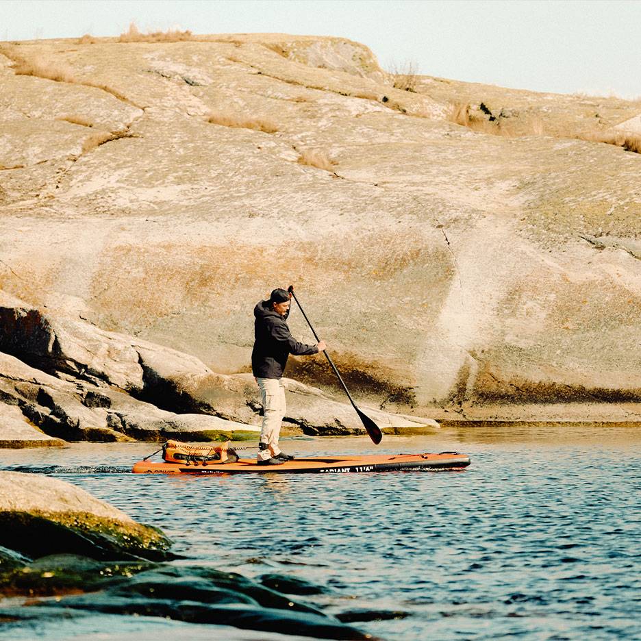 Man paddlar en orange SUP-bräda på en klippig sjö.